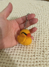 Needle felted yellow duck keychain with orange beak held in palm, showing size and detail