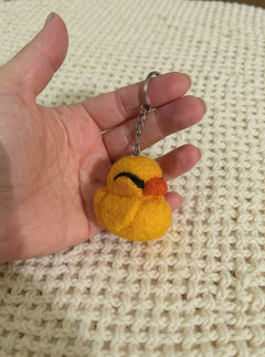 Needle felted yellow duck keychain with orange beak held in palm, showing size and detail