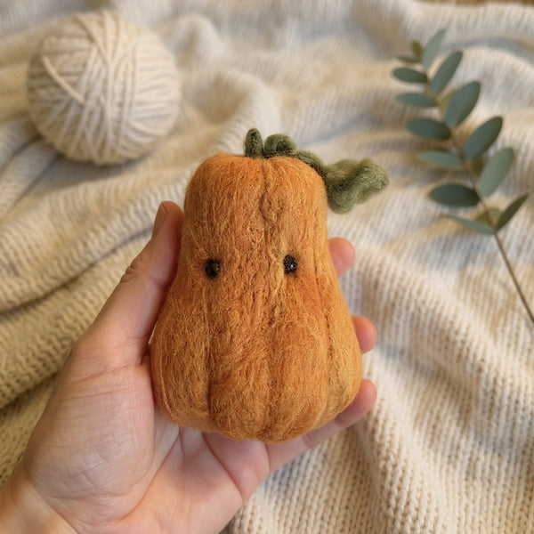 Needle felted butter squash with green stem held in hand, showing size and orange wool texture