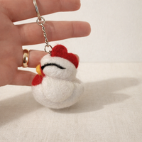 Needle felted chicken keychains displayed on warm cream background