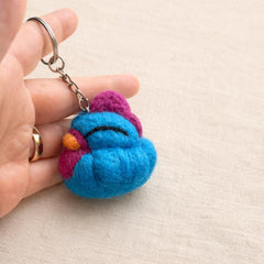 Needle felted owl keychain in blue with magenta and gold details, held in hand showing scale