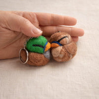 Needle felted duck keychain in brown, green, and blue wool held in palm, showing size and detail