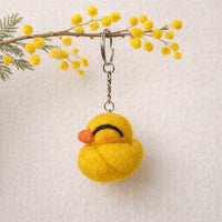 Needle felted yellow duckling keychain hanging from mimosa branch with green foliage