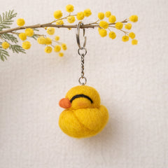 Needle felted yellow duckling keychain hanging from mimosa branch with green foliage