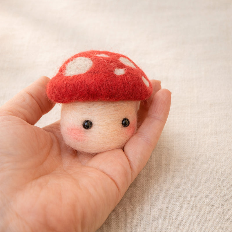 Needle felted red and white mushroom character with cute face held in palm, showing small size