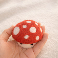 Needle felted red mushroom with white spots and black eyes, held in palm for scale