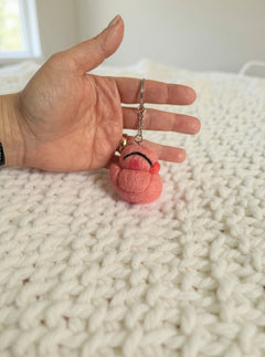 Needle felted pink chicken keychain held in palm, showing tiny size with closed eyes and sweet expression