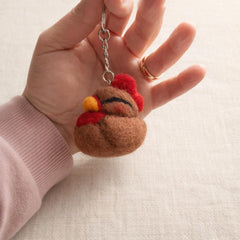 Needle felted robin keychain held in palm, showing red breast, brown wings, and yellow beak details