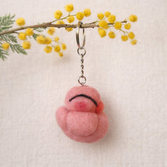 Needle felted pink sleeping chicken keychain hanging from branch with yellow mimosa flowers